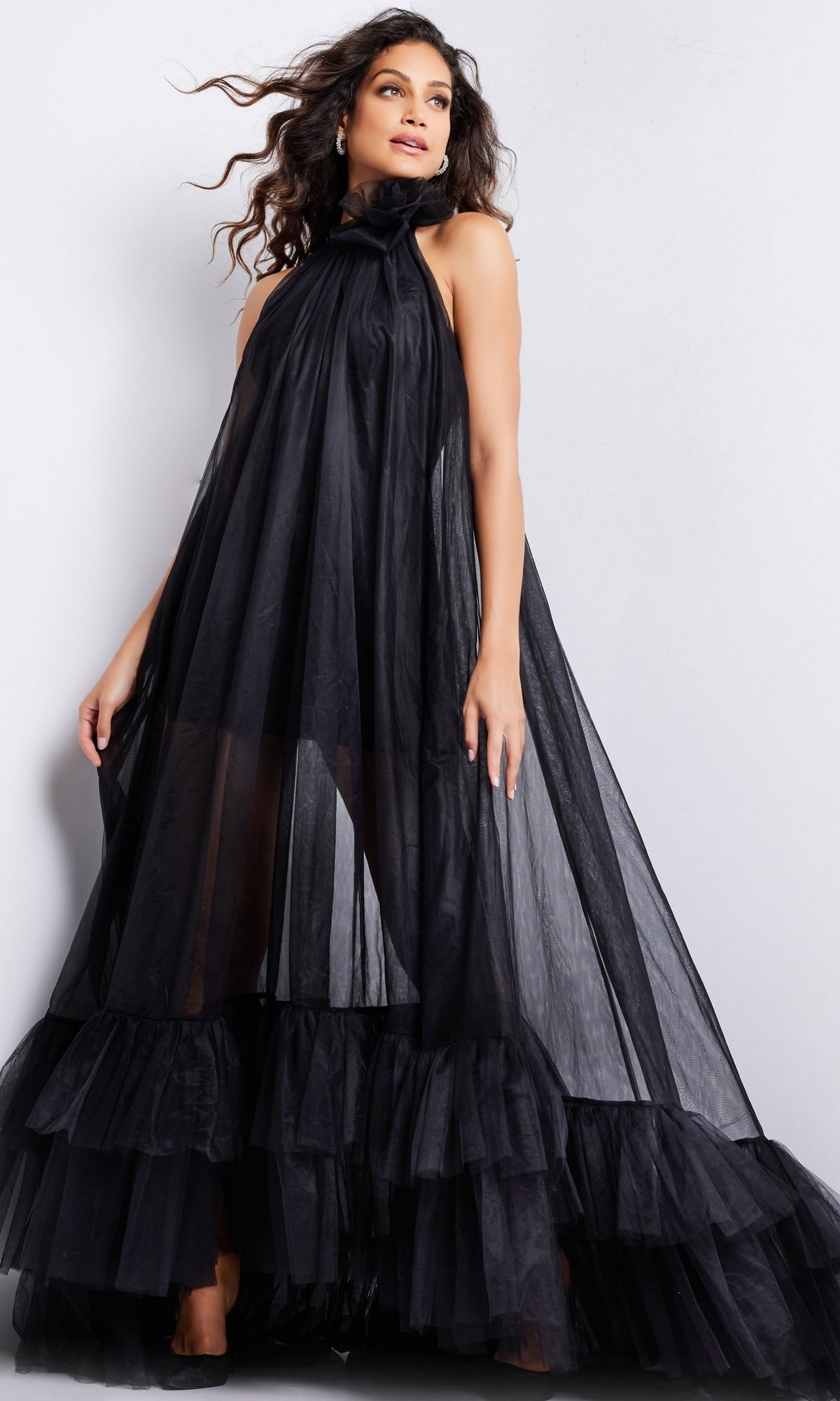 A woman poses against a plain light background wearing the Long Prom Dress 38720 by Jovani, a sleeveless black tulle dress with a sheer high neckline and ruffled hem.
